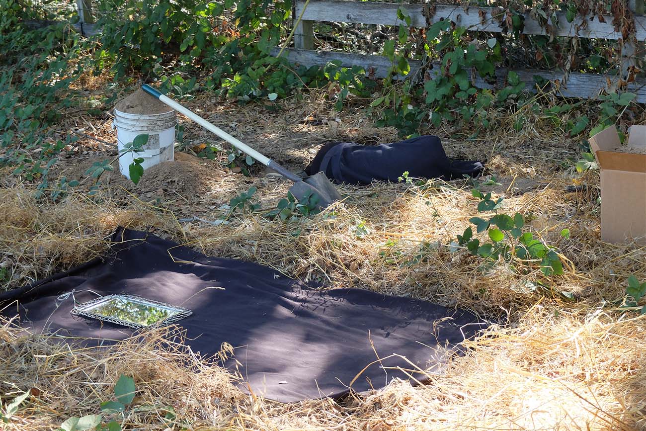 In the foreground, a black cloth covers a cleared rectangle of earth. Marbles Jumbo Radio lies on the ground in the background. In the foreground, a black cloth covers a cleared rectangle of earth. Marbles Jumbo Radio lies on the ground in the background.