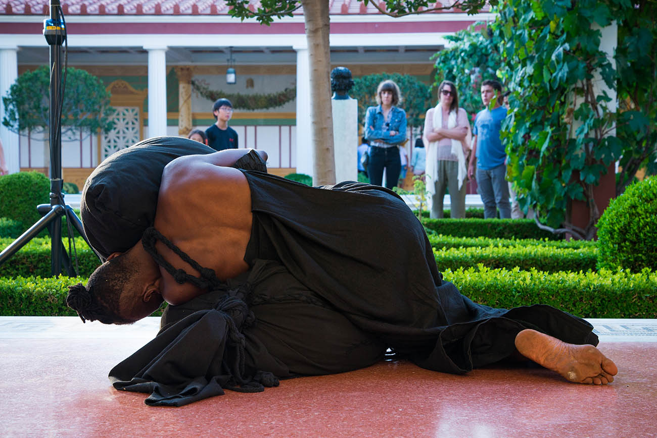 Lying down in the covered walkway of the Getty Villa's Outer Peristyle Garden, taisha paggett embraces the Literal Weight during her performance of Mountain, Fire, Holding Still at the Getty Villa. Lying down in the covered walkway of the Getty Villa's Outer Peristyle Garden, taisha paggett embraces the Literal Weight during her performance of Mountain, Fire, Holding Still at the Getty Villa.