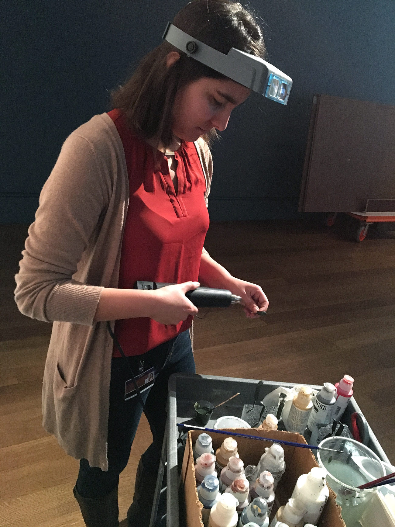 A young woman in a red shirt works with conservation equipment to help install an exhibition at the Getty Center