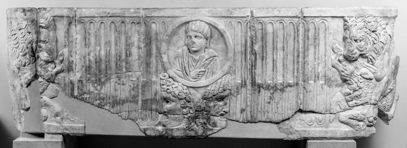 A sculpted marble panel with, in relief, a portrait of person in the center and lions devouring prey on either side.