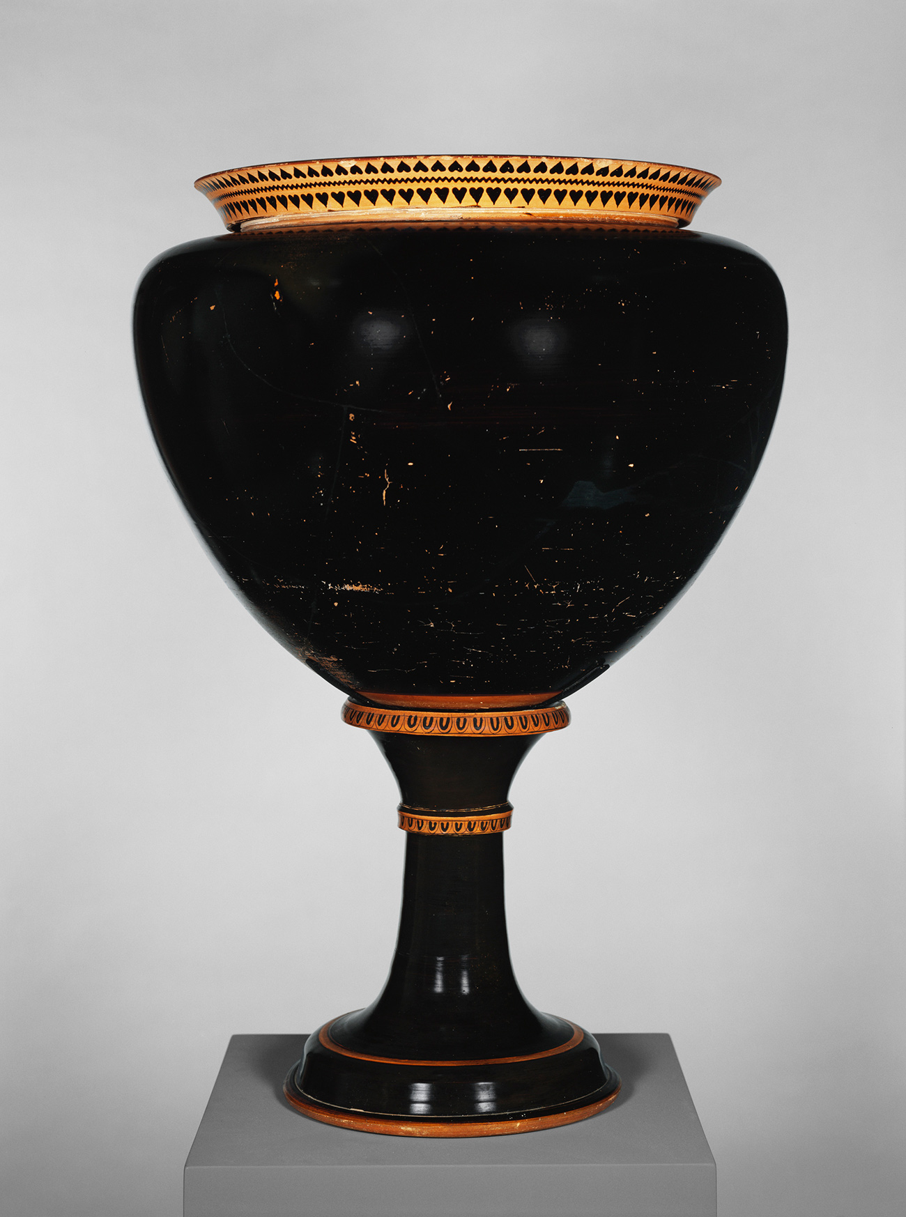 A glossy black, bulbous vase with a terracotta lip atop a tall stand