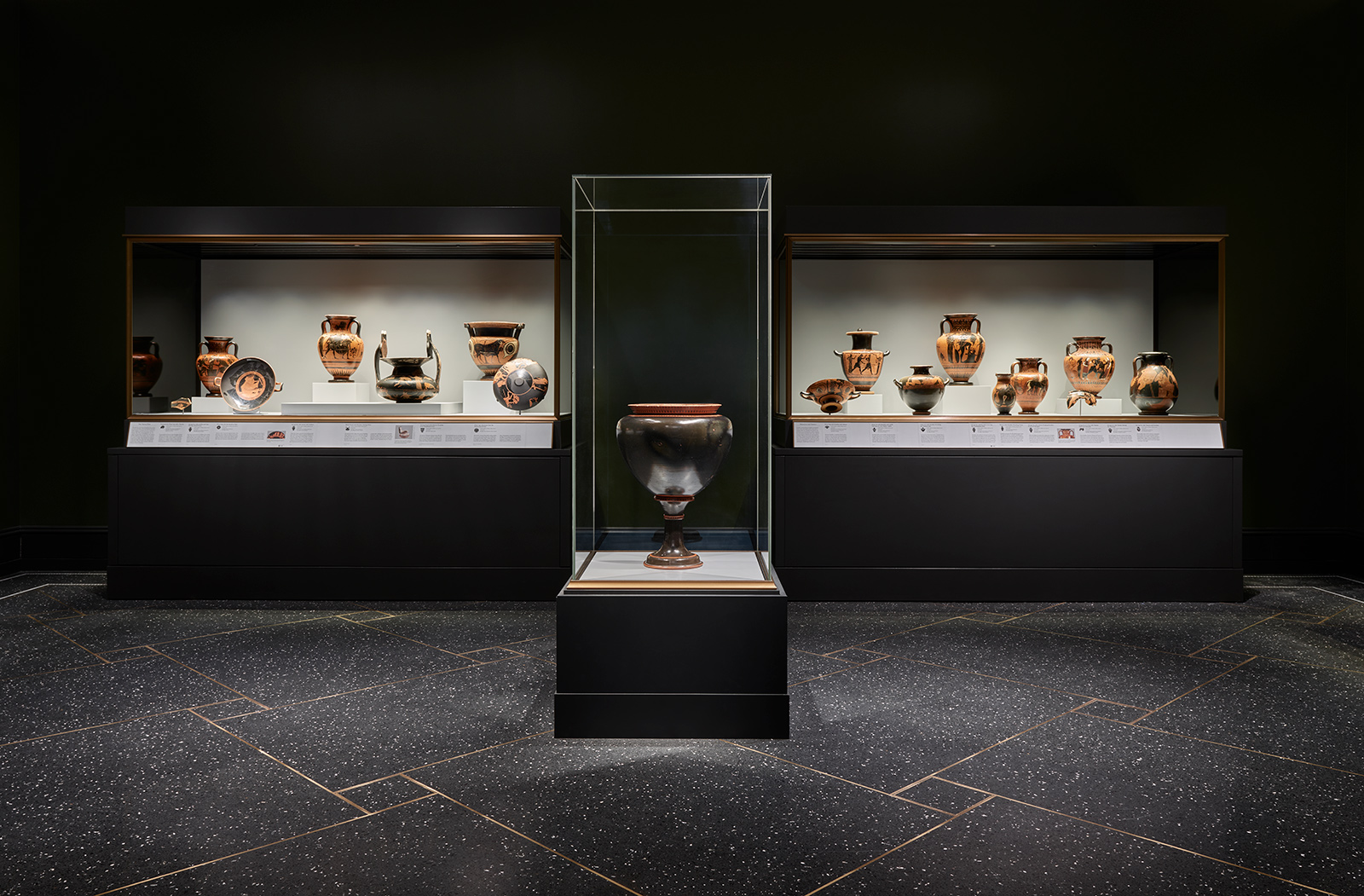 A darkly lit museum gallery with glass cases holding ancient Greek terracotta vessels