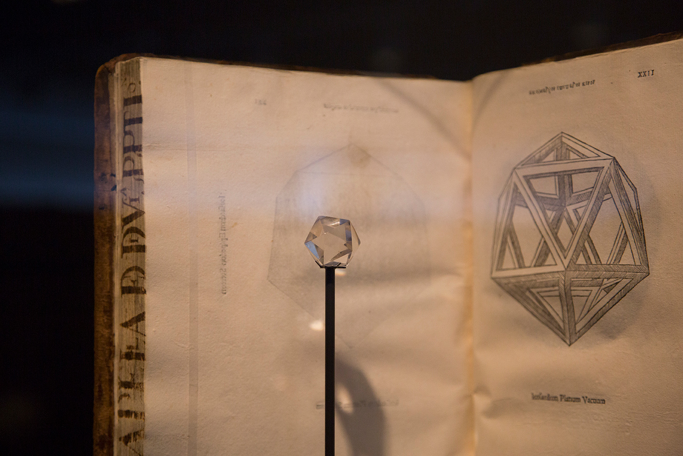 Close-up of an ancient crystal juxtaposed with a Renaissance book showing a schematic of its design